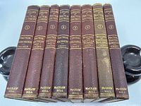 Front view of 8 hardcover books with burgundy spines and gold titles showing volume numbers and titles.