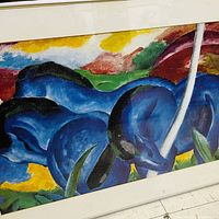 Close-up showing the vivid blue horses and colorful abstract background in the print with part of the white mat and metal frame visible.