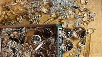 Close-up photo of hundreds of clear and some smoky chandelier crystals mixed in a box and on surface, showing various shapes and facets