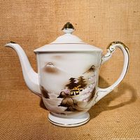 Single view of the teapot showing handpainted village scene with mountain and gold accents on spout, handle, and lid.