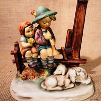 Front and side view of the Hummel figurine showing two children and two dogs in natural setting with wooden fence.