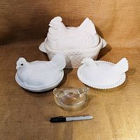 Lot of 4 hen on nest containers of various sizes shown with a marker for scale, including two milk glass hens, one clear glass hen, and a large ceramic dish.