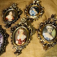 Close-up of four ornate gilt frames with fabric prints of women in historical dress