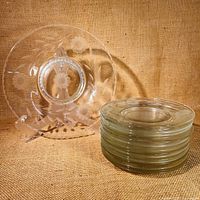 Set of 16 smaller cornflower etched glass plates stacked with one large plate displayed on a stand behind them.