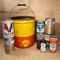 All nine vintage automotive oil and treatment tins displayed together including Shell bucket, Quaker State, Esso Extra, Castrol, Wynn’s, Valvoline, and Canadian Tire.