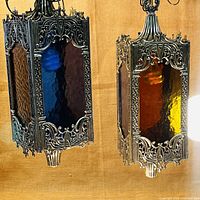 Front and side view of two Moroccan hanging lamps showing blue and yellow/orange textured glass panels and intricate metalwork