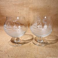 Two scotch glasses with wide rounded bowls featuring etched sailing ship designs on clear crystal.