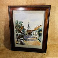 Full view of the framed watercolour painting showing the village street scene in a dark wood frame with mat.