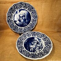Two large decorative Delft charger plates in blue and white with detailed portraits, placed on a textured brown surface.