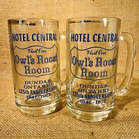 Two clear glass mugs with blue text and gold rims, shown side by side on fabric surface.