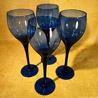 Four cobalt blue slender stemmed wine glasses arranged in group, showing rounded bowls and circular bases.