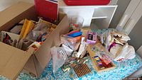Photo showing boxed and bagged arts and crafts supplies including paints, strings, and beads on a table