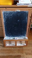 Front-facing view of the used chalkboard with visible wear and storage tray holding chalk pieces.