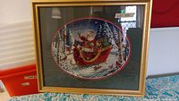 Full view of framed Christmas cross-stitch with Santa Claus in sleigh flying through snowy forest with deer and cardinals.