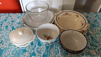 Photo showing assortment of dishes including clear glass bowls, floral and fruit patterned ceramic bowls, and lidded white ceramic dish.