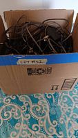 Box filled with various tangled cords and electronic adapters taken to show quantity and condition of cords in the lot.