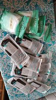 Top-down photo of multiple unopened packages of face masks including green, white and black colored packages lying on patterned fabric surface.
