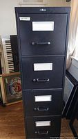 Front view showing all four drawers with handles and label holders on black filing cabinet.