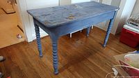 Blue painted wooden table with turned spindle legs showing wear and damage