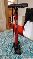 Red manual tire air pump labeled 'lifton' showing upright pump with handle and hose, placed on fabric surface indoors.