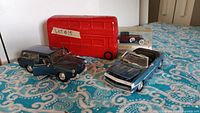 Front and side view of four toy cars and red double-decker bus on patterned cloth