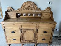 Full front view of chiffonier sideboard showing four lower drawers, central cupboard door, four upper shallow drawers and carved crest.