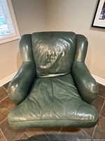 Front view of the green leather armchair showing the cushioned seat and creased back cushion.