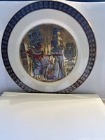 Full view of the decorative plate with detailed Egyptian artwork depicting two figures in royal attire against a gold reflective background, bordered by a blue and gold rim.