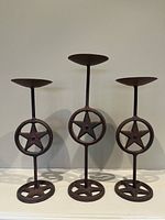 Front view of all three metal rustic candle holders on a white surface against a wall, showing full size and design with star motifs
