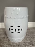 Front view of the white ceramic garden stool showing pierced cutout design and glossy finish.