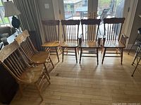 Photo showing set of six rustic pine wood dining chairs arranged in two rows, four armless and two armchairs, light brown finish, visible wear.