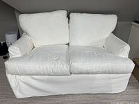 Front view of white fabric loveseat with slipcovers fitted over cushions and base. The loveseat has two seat cushions and two back pillows, slipcover skirt reaches floor.