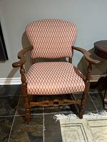 Front view of vintage chair showing orange and white geometric upholstery and wooden frame with curved armrests and ornate legs.