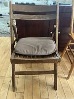 Front view of wooden folding chair with brown fabric cushion showing wear on wood surface and cushion.