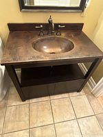 Front view showing dark brown wood vanity with open shelf and cupboard below, hammered brass top with integrated sink and Perrin & Rowe brass faucet.