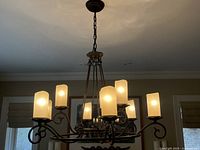 Chandelier hanging from ceiling with nine lit faux candle light shades showing the bronze metal arms and chain mount