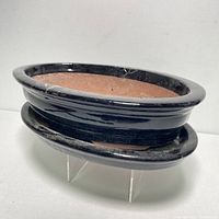 Side angle of black glazed terracotta bonsai planter stacked on drainage tray showing vessel shape and rim.