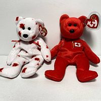 Two official Canadian TY Beanie Babies: one red with Canadian flag patch, one white with red maple leaves.