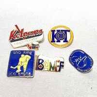 Five Canadian sports-themed pins: Kelowna Minor Hockey shaped like a hockey stick and puck, Kingston 2D Donnacona Minor Hockey round pin, Sno King Ice Arena rectangular blue pin with hockey player figure, colorful BAMF pin, blue Vancouver Basketball pin with player silhouette.