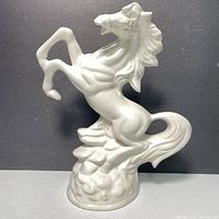 Left side view of the glossy white ceramic horse figurine showing muscular details and textured base.