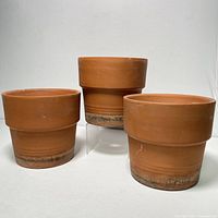 Lot of three large terracotta clay planter pots shown from front with visible wear at base