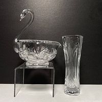 Photo showing clear crystal swan dish with a curved neck and head alongside a tall crystal bud vase with vertical etched cuts.