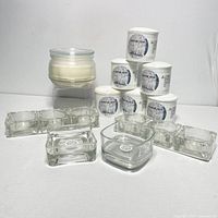 Lot showing seven white scented candles labeled 'VINTER 2016' plus several clear glass candle holders including rectangular and rounded square designs.