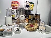 Photo showing Drew Barrymore blender parts, Coggelettes egg boiler box, spice rack with jars, kitchen utensils on wooden holder, knife set, and other boxed kitchen items.