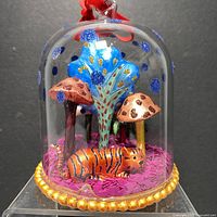 Front view of glass cloche showing mushrooms, blue tree, and tiger on pink confetti base.