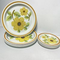 Stack of 4 large dinner plates and 4 smaller side plates showing floral yellow flower design with green leaves and orange-brown rim.