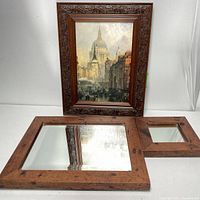 Three rosewood framed items on a white surface: one large rectangular mirror, one smaller square mirror, and a framed art print showing a city street scene with a domed building in the background.