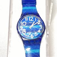 Front view of blue Swatch watch with white Arabic numerals inside clear plastic case.