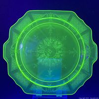 Full view of the octagonal uranium glass serving platter glowing bright green under UV light showing etched patterns and handles.