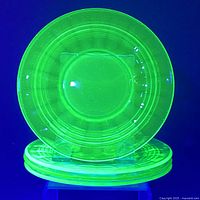Side plates stacked with one plate displayed upright under UV light showing bright yellow-green uranium glass and spider web pattern details.